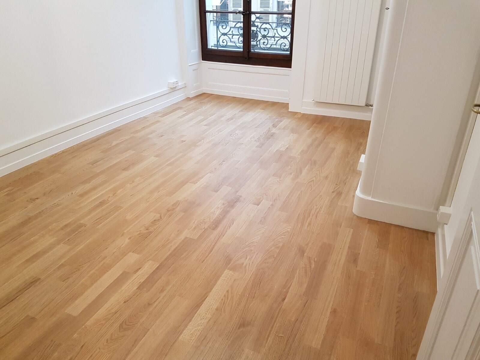 Parquet clair posé dans une pièce vide devant une fenêtre à garde-corps ancien