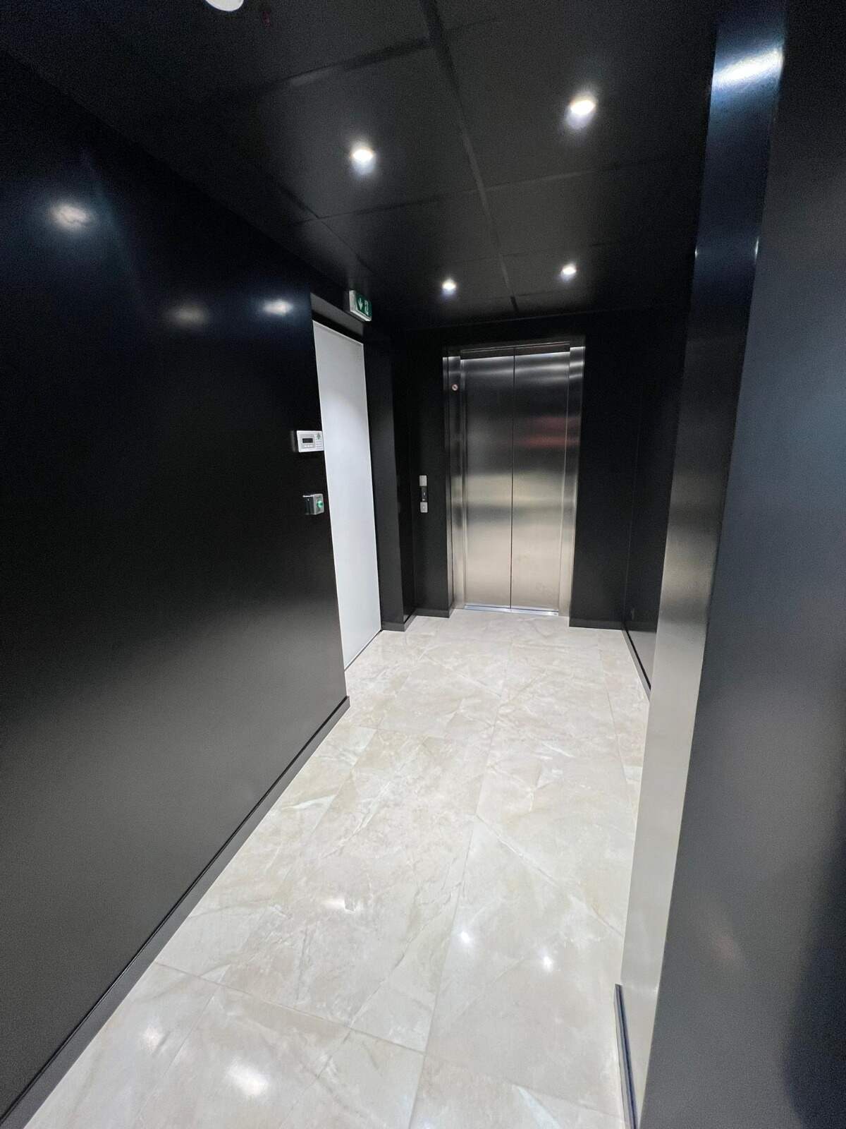 Palier d'immeuble avec porte d'ascenseur, plafond sombre et sol en pierre claire