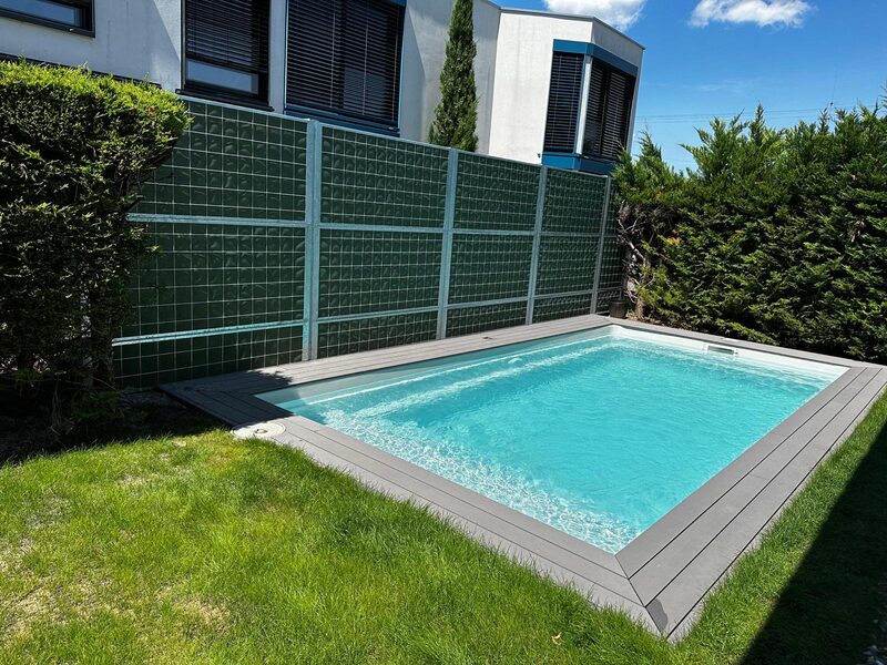 Piscine enterrée avec margelles claires bordée de gazon et d'une clôture