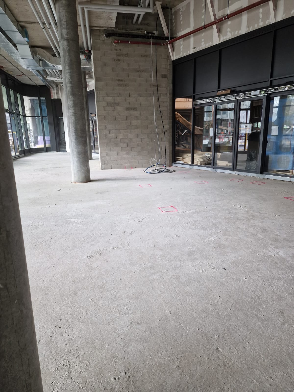 Local commercial brut avant aménagement à Genève : dalle béton, structure et réseaux apparents, devanture vitrée posée