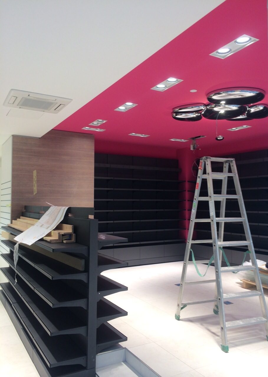 Rayonnages noirs et faux-plafond coloré à spots encastrés dans une boutique en aménagement à Genève